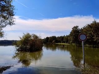 No entry with car. Overflowed pond next to park. Flood in Czech Republic. Road under water. Large amount of water. Disaster in Czech. Climate change. Clear blue sky after heavy rain. Weather in autumn