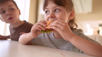 children eat burgers. fast food burger. a group of small children in the kitchen greedily eat fast food burgers. big family sun small kids having breakfast in the morning in the kitchen eating burger