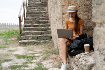 Woman travel blogger editing photos on laptop at ancient fortress