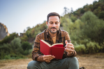 Adult caucasian man sit in front tent and read book on camping trip