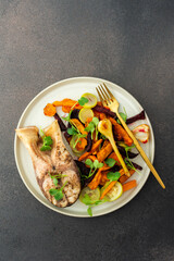 Enjoy baked silver carp with roasted vegetables like carrots, zucchini, beets, and garlic for a nutritious and tasty breakfast or lunch, plates with food on a dark background