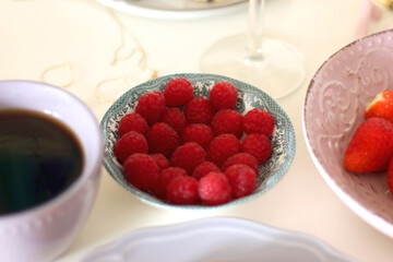 Plate of pastel macarons, cookies and chocolate, cup of tea of coffee, glass of bubble water, various berries, books and accessories on the table. Selective focus, pastel colors.