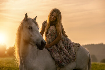 Obraz premium Romantic horsemanship portrait: A young woman and her icelandic horses interacting together in front of a beautiful sunrise landscape