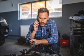 mechanic inspect car engine with tool at garage and talk on cellphone