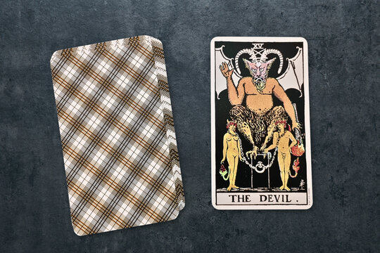 Carte de tarot "Le Diable" du jeu Rider-Waite, symbolisant la tentation et les d&eacute;sirs mat&eacute;riels. Carte sur fond gris textur&eacute; &agrave; c&ocirc;t&eacute; d'une autre carte face cach&eacute;e.