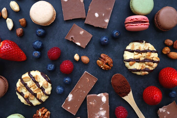 Macarons, chocolate, cookies, berries and various nuts on dark blue background. Top view.