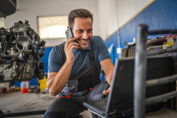 Car mechanic work on laptop while talk on mobile phone in garage