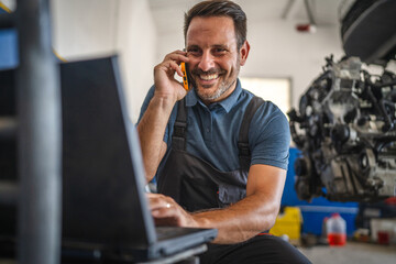 Car mechanic work on laptop while talk on mobile phone in garage