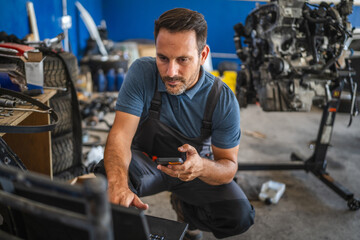 Car mechanic inspect engine, use a laptop and mobile phone in garage