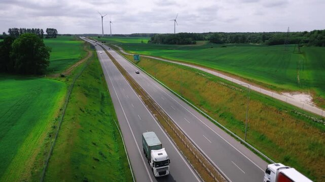 Modern European autobahn. Wide multi-lane highway with passing trucks and cars against the background of wind generators. Aerial view. High quality 4k footage
