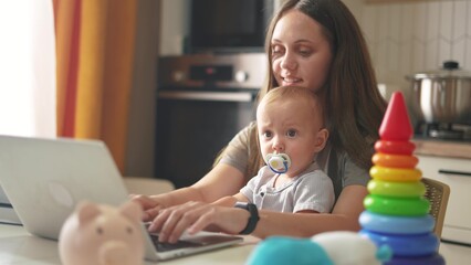 mother with a child sits at a table and works on a laptop. remote work mom baby concept. a woman works lifestyle in a family setting on the table are her child's toys. computer work