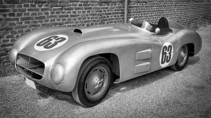An old, silver vintage racing car with an aluminum body in a minimalist black-and-white photograph.