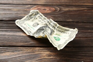 One crumpled dollar banknote on wooden table, closeup