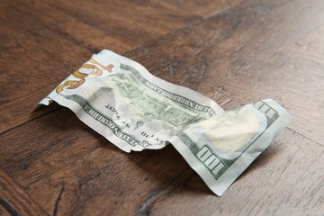 One crumpled dollar banknote on wooden table, closeup