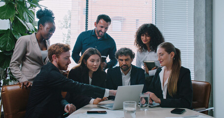 Multi-ethnic group of people listening carefully to woman sitting in front of computer. Consulting together about difficult decision for business company. Working together. Looking at laptop monitor.