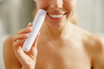A cheerful woman beams with joy as she confidently holds a skincare device, highlighting her skincare routine