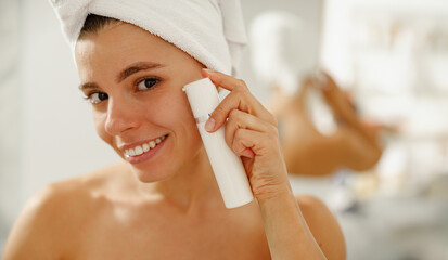A woman happily applying her skincare product while smiling, showcasing her enjoyable and fresh...
