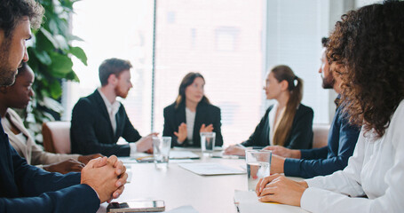 Charming Asian female in business suit Consulting with team in defocus background. Standing in front of her colleagues and making important announcement. Describing problem and expecting advices.