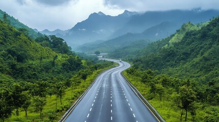 Obraz premium A scenic view of a long stretch of motorway winding through mountains, with lush greenery on either side, showcasing the beauty of road travel.