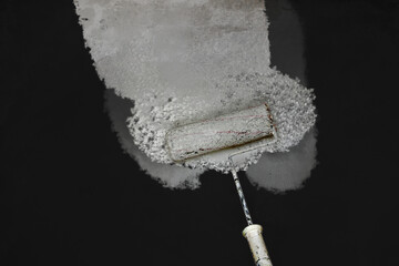 Creative graphic concept of paint roller applying fresh white paint onto the black color concrete...