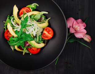 Fresh vegan salad with avocado, tomatoes and cucumber in black plate