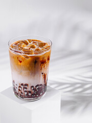 Iced coffee latte with chocolate syrup standing on white cube with tropical leaf shadow