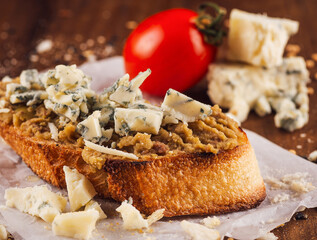 Toasted baguette with pate, blue cheese and tomato on wooden table