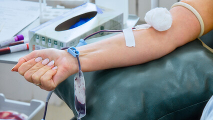 A person is shown donating blood, with a collection tube drawing blood from their arm into a blood...