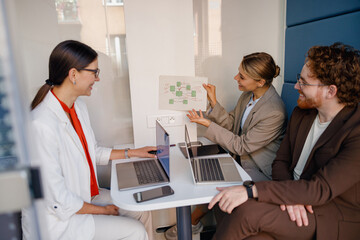Obraz premium In a modern office, a diverse team engages in discussions about innovative projects using laptops and visual aids