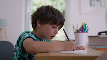 Naklejka premium Child concentrating on his artwork, pencil in hand, surrounded by coloring supplies, engaged in creative activity at home, natural light from a nearby window