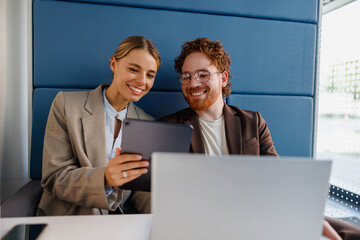 Two enthusiastic young professionals are collaborating on a tablet together in a stylish and modern...