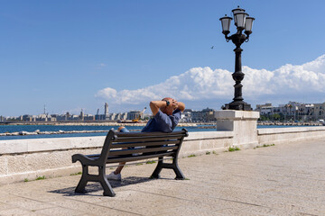 Man resting on a bench at Emperor Augustus seafront (Lungomare Imperatore Augusto), promenade by...