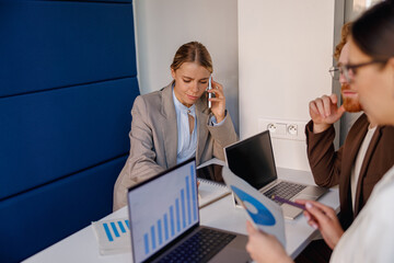 A professional team is engaged in a strategic business meeting using laptops and charts for discussions