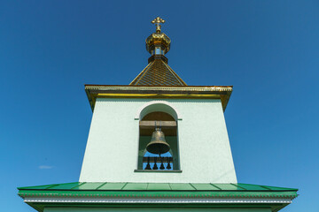 View of the bell tower and the dome with the cross of the Christian church. An old bell tower made of white stone and a large cast-iron bell hanging on a wooden beam.