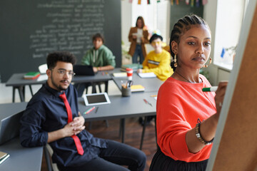 Black young woman using flip chart during seminar in school classroom with students and teacher...
