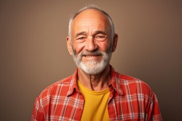 Obraz premium Portrait of a grinning man in his 70s dressed in a relaxed flannel shirt in front of solid color backdrop
