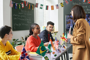 Side view at female teacher talking to group of students during international conference in school classroom