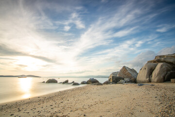 View through rocks on a sandy beach into the sunset. Landscape shot with a view to the horizon over...