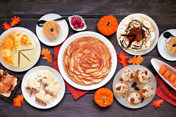 Autumn desserts table scene with a variety of gourmet fall sweet foods. Top down view over a dark wood background.