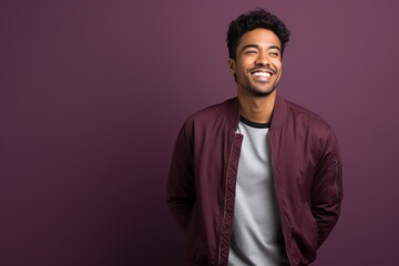 Fototapeta premium Portrait of a satisfied indian man in his 20s wearing a trendy bomber jacket over solid color backdrop