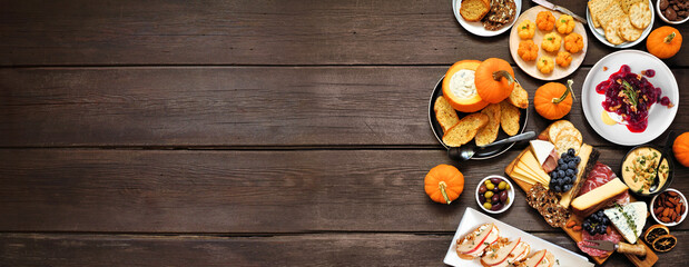 Autumn theme appetizer side border against a dark wood banner background. Charcuterie board, pumpkin and apple dips, crostini, cheeses and snacks. Above view.