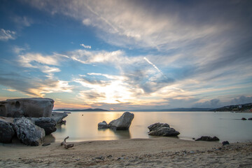 View through rocks on a sandy beach into the sunset. Landscape shot with a view to the horizon over...
