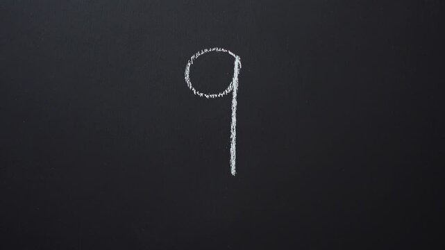 Hand writes the number 9 with white chalk on a black board
