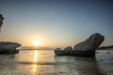View through rocks on a sandy beach into the sunset. Landscape shot with a view to the horizon over...