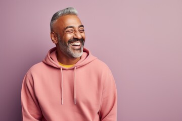 Obraz premium Portrait of a joyful indian man in his 50s sporting a comfortable hoodie while standing against solid pastel color wall