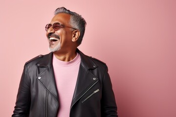 Obraz premium Portrait of a cheerful indian man in his 50s sporting a stylish leather blazer while standing against solid pastel color wall