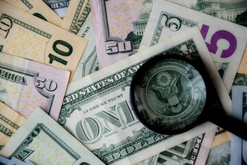 Big amount of US dollar bills in different nominations and magnifying glass. Many dollar banknotes...