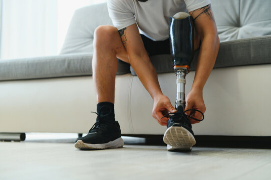 Man amputee with prosthetic leg disability on above knee transfemoral leg prosthesis wearing shoe sitting on sofa, close up. People with amputation disabilities everyday life concept