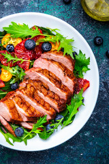 Foodie food salad with grilled duck and bloody orange, kumquat, blueberry and lettuce on blue background, top view