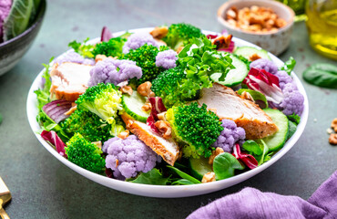 Healthy food salad with cauliflower, broccoli, chicken, cucumber, onion, radicchio, spinach with walnuts, green background, top view